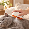 Owner gently brushing a relaxed grey cat with the SpaMist mist brush on a sofa